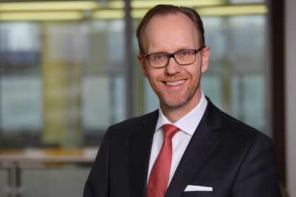 Portrait von Henning Lobin. Er trägt ein weißes Hemd, eine rote Krawatte sowie einen schwarzenn Blazer und lächelt.