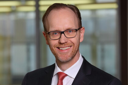 Portrait von Henning Lobin. Er trägt ein weißes Hemd, eine rote Krawatte sowie einen schwarzenn Blazer und lächelt.