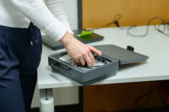 Kleiner grauer Koffer liegt auf dem Tisch, aus dem mit beiden Händen Kabel entnommen werden