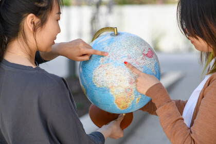 Zwei Studierende deuten mit ihren Zeigefingern auf einen Globus.