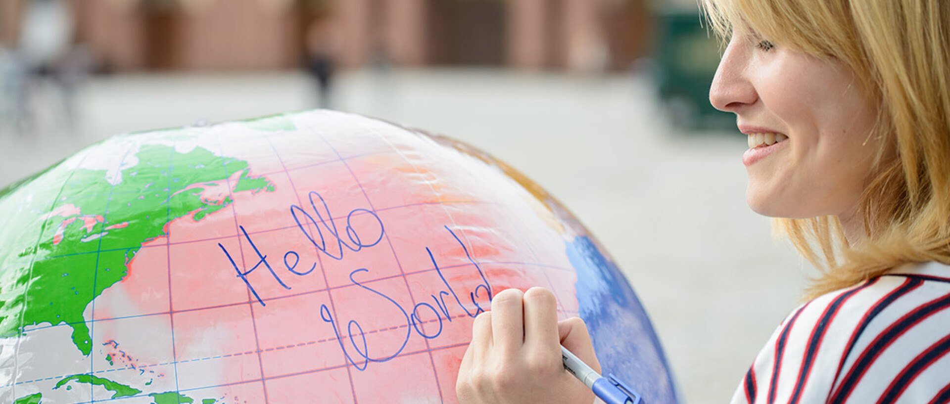 Eine junge Frau schreibt auf eine Weltkugel die Wörter "Hello World".