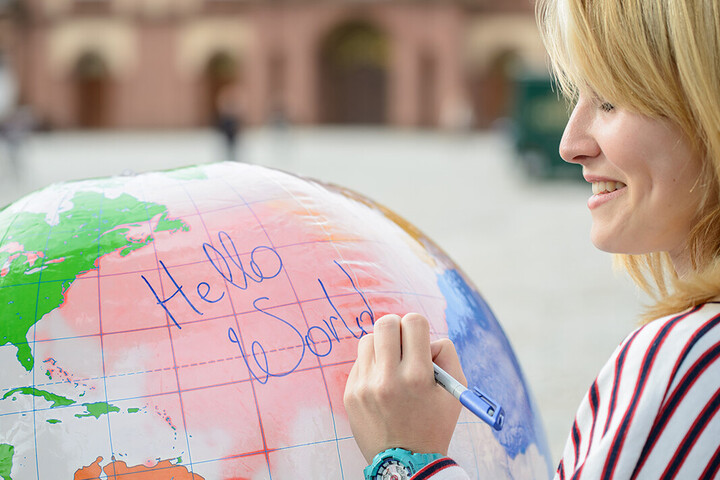 Eine junge Frau schreibt auf eine Weltkugel die Wörter "Hello World".
