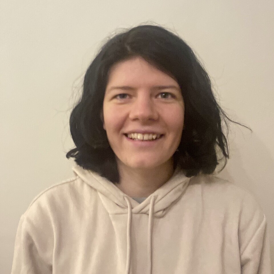 Lea Cohausz hat schulterlange schwarze Haare. Sie trägt einen cremefarbenen Kapuzenpullover und steht vor einer hellen Wand.