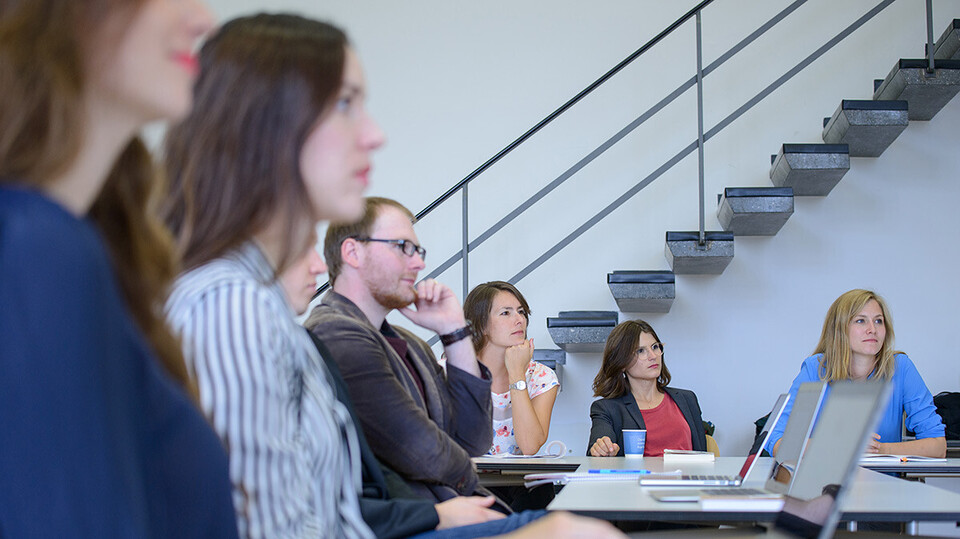 Junge Frauen und Männer sitzen mit ihren Laptops in einem Seminarraum.