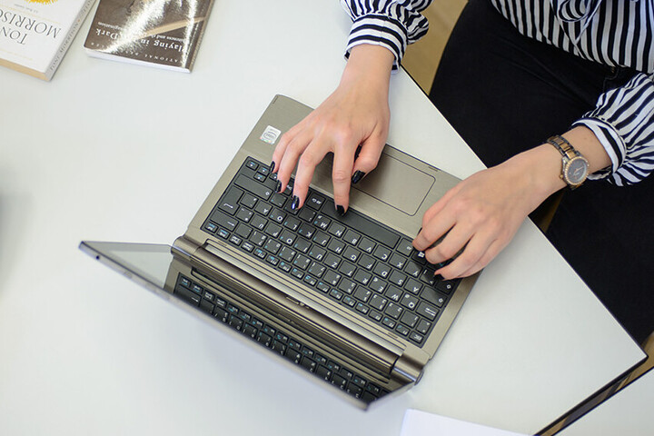 Ein aufgeschlagener Laptop steht auf dem Tisch und zwei Hände tippen darauf. 
