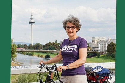 Susanne Quincke hat kurze graue und lockige Haare. Sie trägt eine Brille und ein lilanes T-Shirt. Sie hält ein Fahrrad fest und blickt lächelnd in die Kamera. Oben links steht "Green Uni Ma".