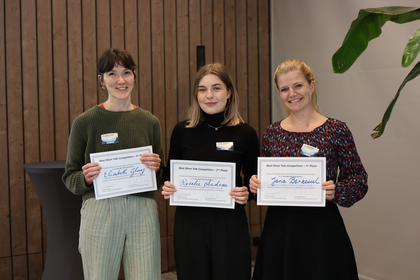 Drei Frauen stehen neben einander und halten Urkunden in den Händen.