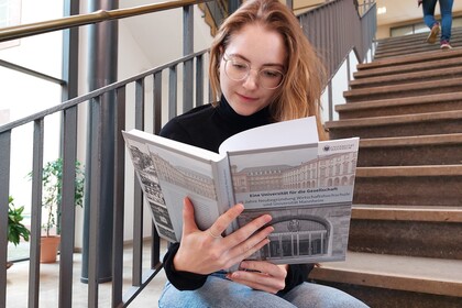 Eine Studentin sitzt auf Treppenstufen und liest in einem Buch über die Universität Mannheim. 