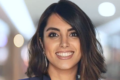 Portrait of Gholami Behnaz. She is wearing a blue blazer and standing in an office.