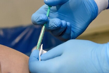 Nahaufnahme einer Impfung. Eine Person mit blauen Handschuhen hält eine Spritze in der Hand.