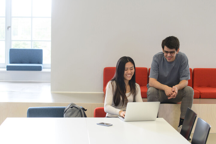 Zwei Studierende sitzen lachend vor einem Laptop.