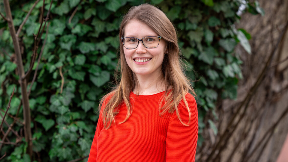 Julia Freimuth. Julia Freimuth lächelt breit und trägt ein rotes Oberteil und Brille.
