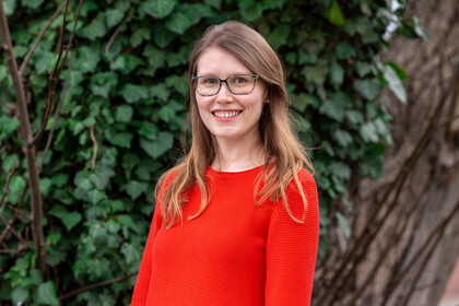 Julia Freimuth. Julia Freimuth lächelt breit und trägt ein rotes Oberteil und Brille.