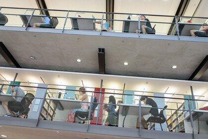 Studierende sitzen auf verschiedenen Etagen der Bibliothek an Arbeitsplätzen.