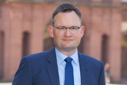 Portrait von Philipp Gassert. Er trägt einen blaugrauen Anzug mit blauer Krawatte. 