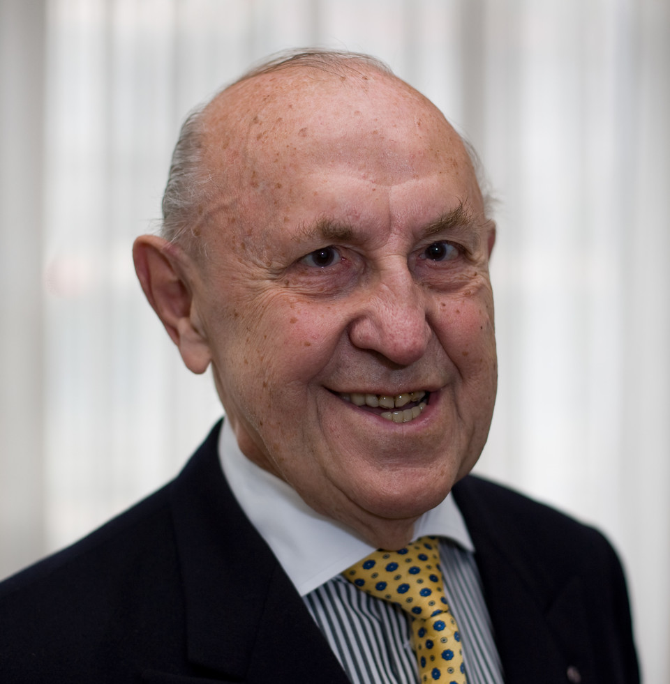 Portrait von Hans Raffee. Er trägt einen schwarzen Blazer mit gelb-braun gepunkteter Krawatte. 