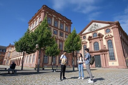 Blick auf den Ostflügel der Universtät Mannheim. Drei Studierende stehen davor und unterhalten sich.