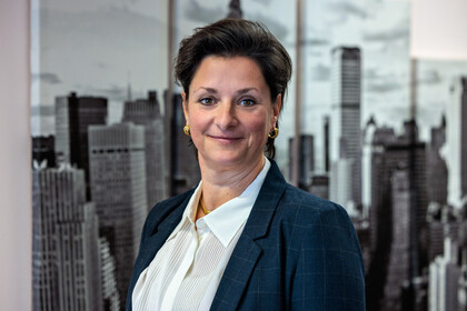 Portraitfoto von Prof. Dr. Stefanie Schäfer vor einem Bild einer Skyline. Sie trägt eine weiße Bluse und einen dunkelblauen Blazer. 