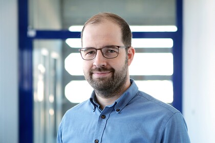 Dr. Lars Leszczensky hat einen Bart und kurze braune Haare. Er trägt ein blaues Hemd.