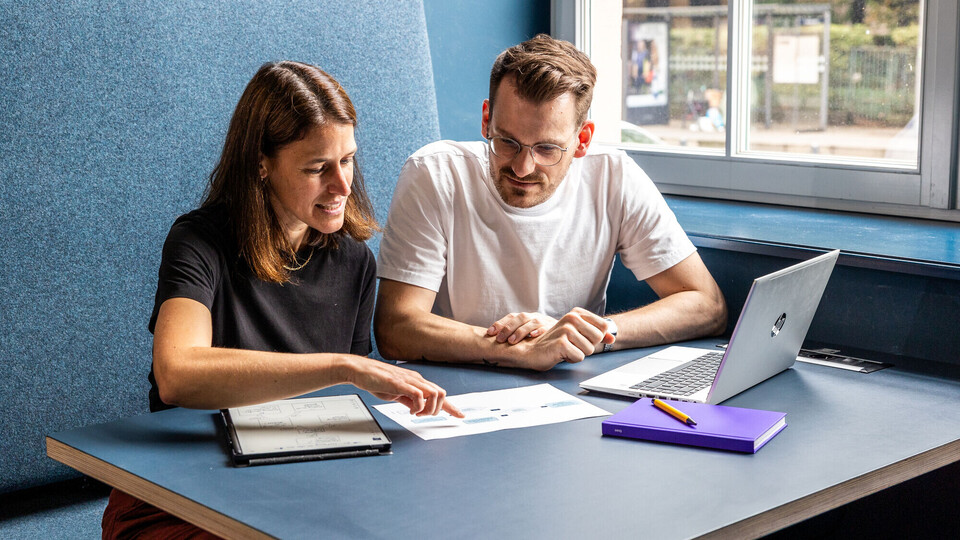 Zwei Studierende sitzen nebeneinander vor einem Laptop.