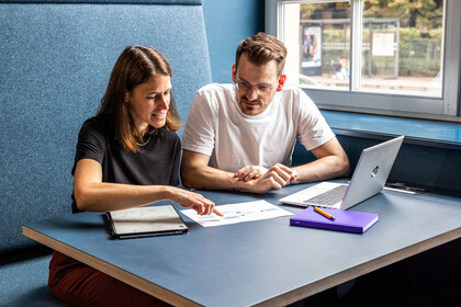 Zwei Studierende sitzen nebeneinander vor einem Laptop.