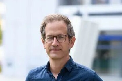 Portrait von Marc Helbling. Er trägt ein blaues Hemd und steht auf einer Grünfläche.