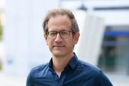 Portrait von Marc Helbling. Er trägt ein blaues Hemd und steht auf einer Grünfläche.