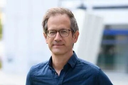 Portrait von Marc Helbling. Er trägt ein blaues Hemd und steht auf einer Grünfläche.