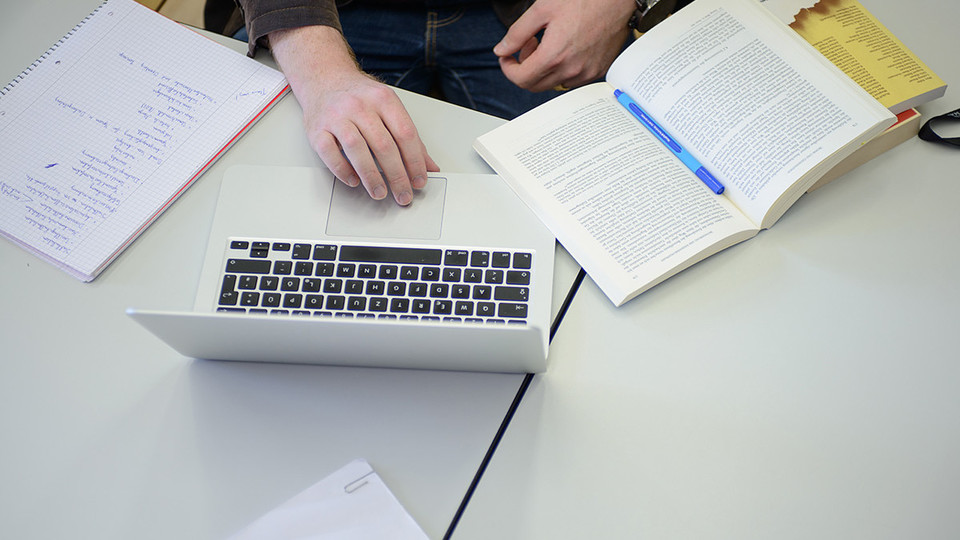Ein Student sitzt mit Büchern und seinem Laptop an einem Tisch.