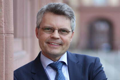 Portrait von Ralf Müller-Terpitz. Er trägt ein weißes Hemd, eine blaue Krawatte sowie einen dunkelblauen Blazer und steht vor dem Schloss.