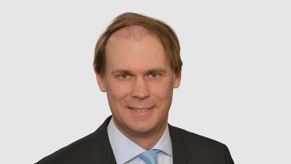 Prof. Bischof hat kurze Haare und trägt ein dunkles Jacket, ein helles Hemd und eine türkisfarbene Krawatte.