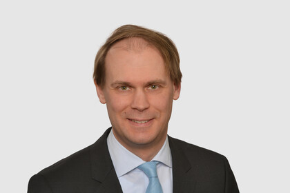 Prof. Bischof hat kurze Haare und trägt ein dunkles Jacket, ein helles Hemd und eine türkisfarbene Krawatte.