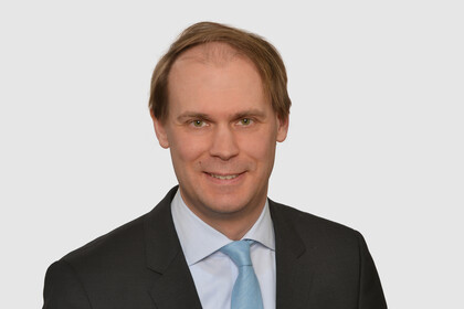 Prof. Bischof hat kurze Haare und trägt ein dunkles Jacket, ein helles Hemd und eine türkisfarbene Krawatte.