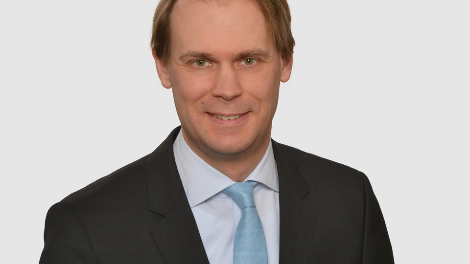 Prof. Bischof hat kurze Haare und trägt ein dunkles Jacket, ein helles Hemd und eine türkisfarbene Krawatte.