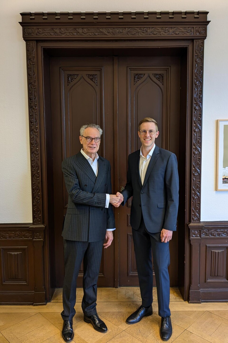 Dekan Joachim Lutz und prof. Dr. Jens Förderer stehen vor einer verzierten Holztür und geben sich die Hand