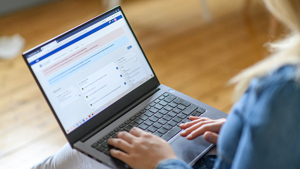 Eine junge Frau hat ihren Laptop auf dem Schoß und arbeitet.