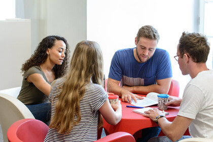 Vier Studierende sitzen an einem runden Tisch und lernen gemeinsam.