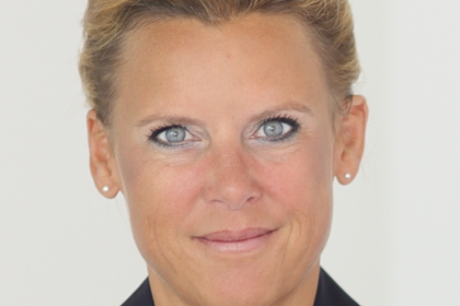 Portrait von Beatrice Rammstedt. Sie trägt eine schwarze Bluse und steht vor einer weißen Wand.