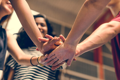 mehrere Menschen strecken ihre Arme in die Mitte und legen ihre Hände aufeinander