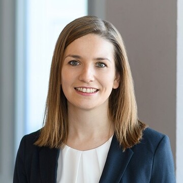 Portrait von Janina Heker. Sie trägt einen dunklen Blazer und eine weiße Bluse.