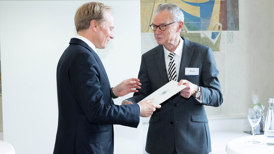 Dekan Lutz überreicht einer Person im Anzug eine Urkunde
