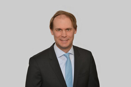 Portrait von Jannis Bischof. Er trägt ein weißes Hemd, eine hellblaue Krawatte und ein schwarzes Sakko.