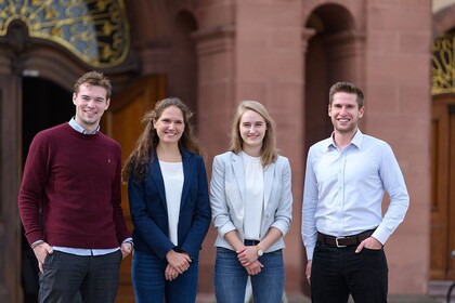 Vier Studierende stehen vor einem Eingang der Universität Mannheim. 