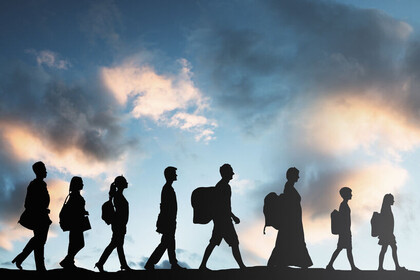 Im Vordergrund sind Silhouetten von acht hintereinanderlaufenden Personen. Hinter ihnen ist ein blauer Himmel mit Wolken. 