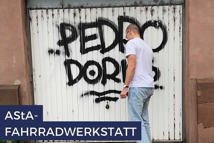 Student steht vor einer alten Garage. Die Garagenwand ist mit Graffiti besprüht. Link: Instagram Fahrradwerkstatt AStA