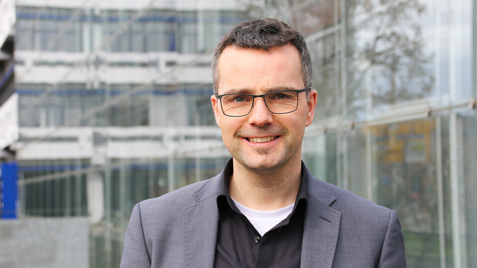Porträt von Prof. Debus. Er steht vor dem Gebäude A5 und trägt kurze Haare, eine Brille und ein graues Sacko.
