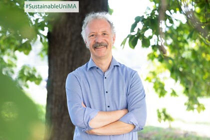 Prof. Dr. Moritz Fleischmann. Er lächelt, sein Hemd ist hellblau gestreift und er hat einen Schnurrbart.
