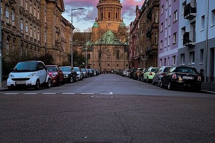 Entfernter Blick auf den Wasserturm in Mannheim. Im Vordergrund ist eine Straße mit Gebäuden und parkenden Autos zu sehen.