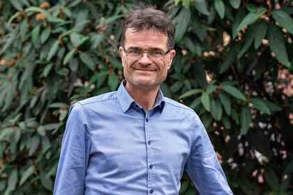 Bernward Gesang. Bernward Gesang trägt ein blaues Hemd und steht vor einem grünen Hintergrund.
