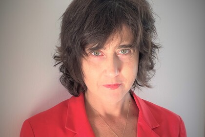 Irena Kogan trägt eine rote Bluse und schaut in die Kamera.